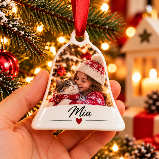 Cloche de Noël en céramique tenue en main, avec la photo d'une petite fille câlinant un chat et le prénom Mia