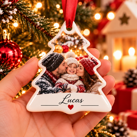 Décoration en forme de sapin en céramique tenue en main, avec une photo de famille, parents embrassant leur enfant, et le prénom Lucas
