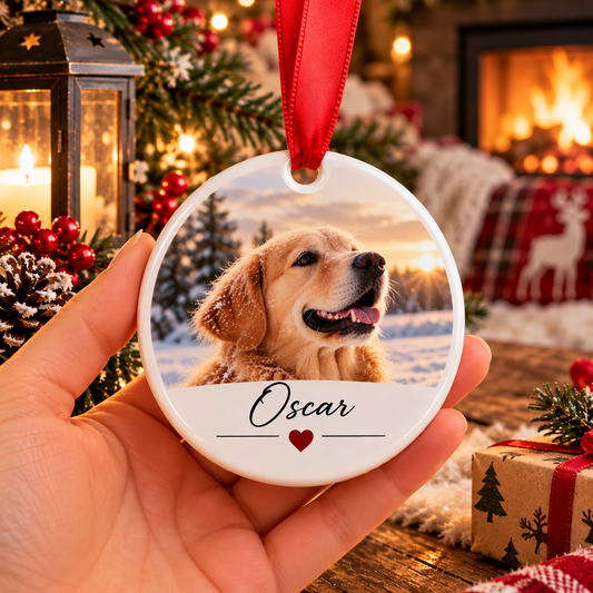 Boule de Noël ronde en céramique tenue en main, avec la photo d'un chien au pelage doré dans la neige et le prénom Oscar